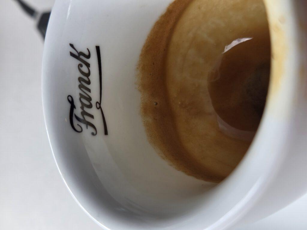 Ein weißer Kaffeebecher mit dunklem Kaffee und dem Schriftzug 'Franck'.