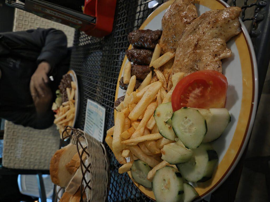 Teller mit gegrilltem Fleisch, Pommes und Salat auf einem Tisch.