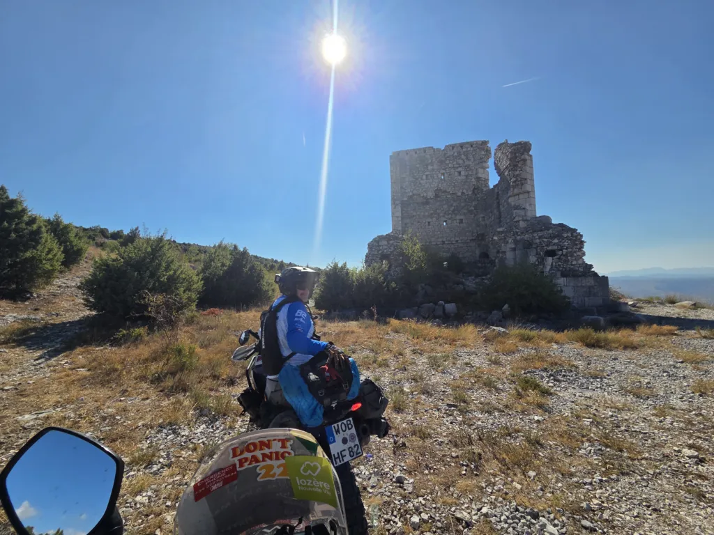 Reiseenduro vor einer Ruine mit Blick auf eine Hügellandschaft, die Sonne blendet.